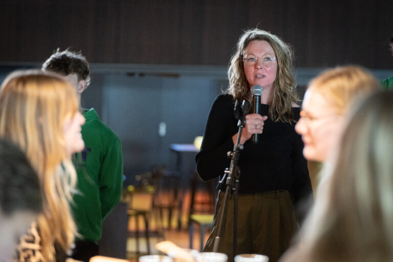Persoon met zwarte trui vertelt met microfoon aan een groep studenten