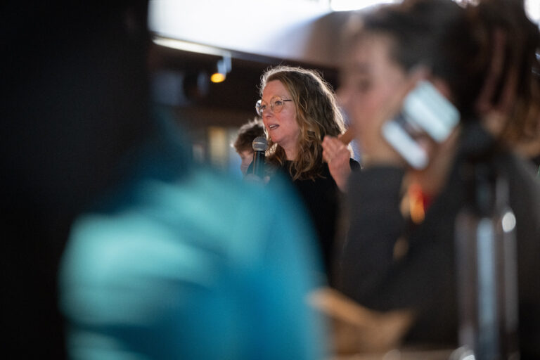 Persoon in zwarte trui vertelt met microfoon aan groep studenten