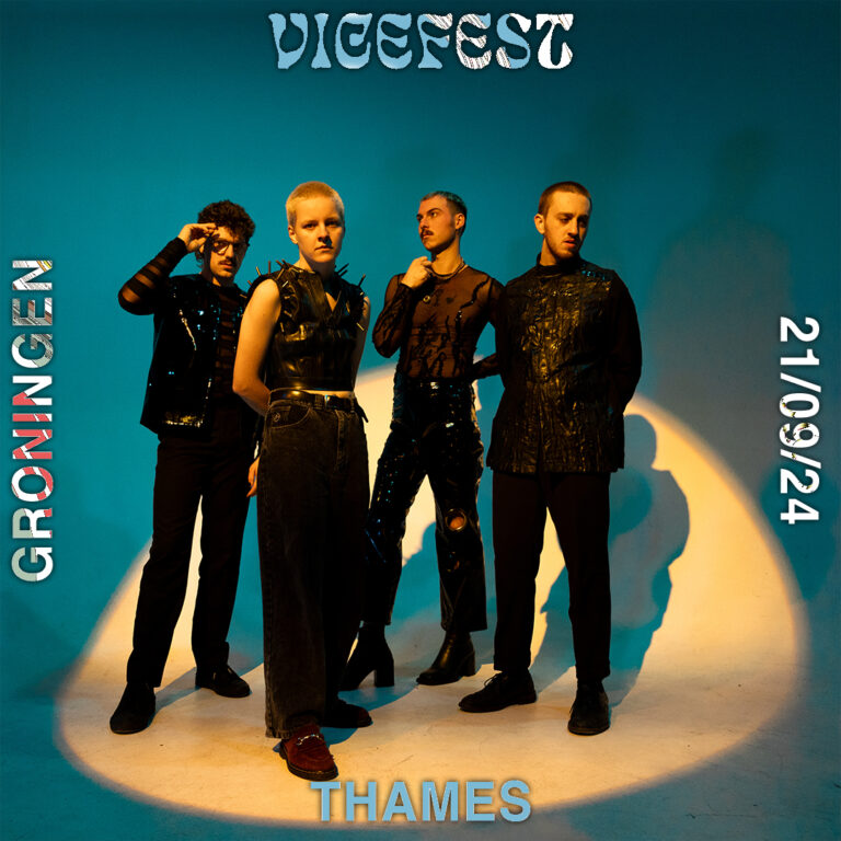 Vier bandleden in zwarte punkkleding staan stoer met gele schijnwerper op ze met blauwe achtergrond.