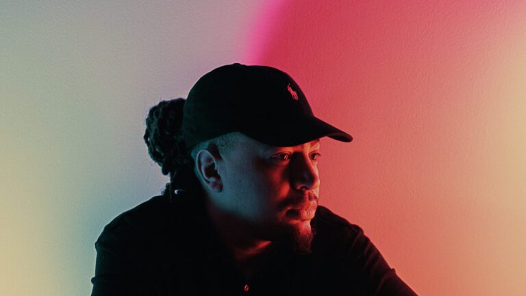 Fresku zit met pet op en armen gekruist leunend op zijn eigen spiegelbeeld voor een kleurrijke achtergrond