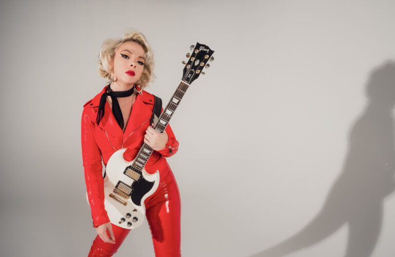 Blonde vrouw met rock gitaar en rood leren pak
