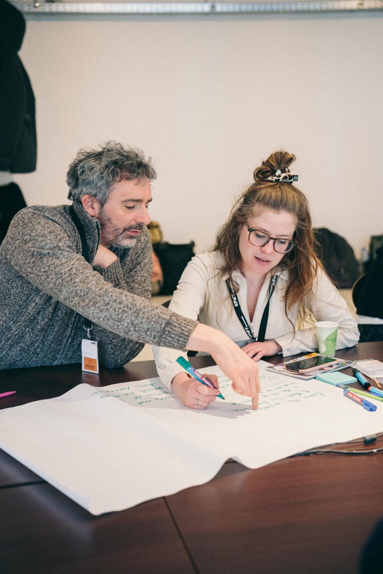 man met grijze trui en vrouw met witte blouse schrijven op papier