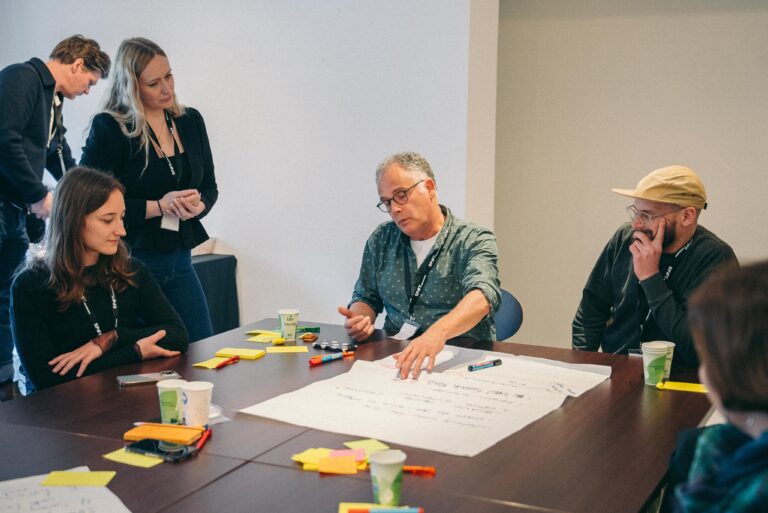 vijf mensen en een man wijst dingen aan op wit papier