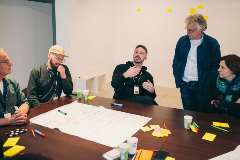 zes mensen aan een tafel met wit papier op tafel