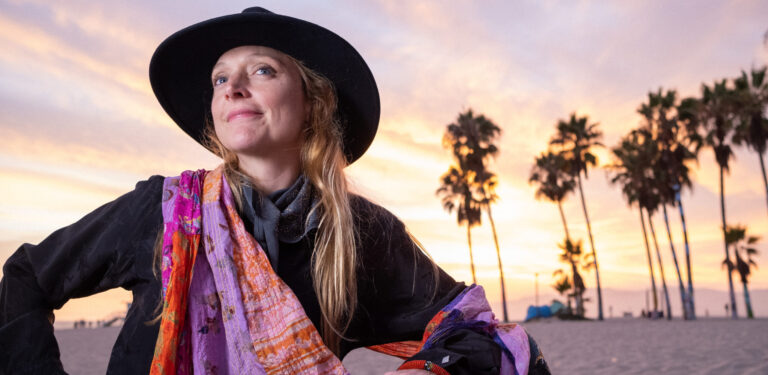vrouw met zwarte hoed en lang blond haar met gekleurde sjaal