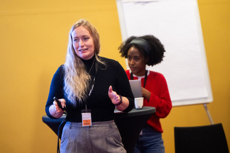 een vrouw met zwarte trui voor een gele muur