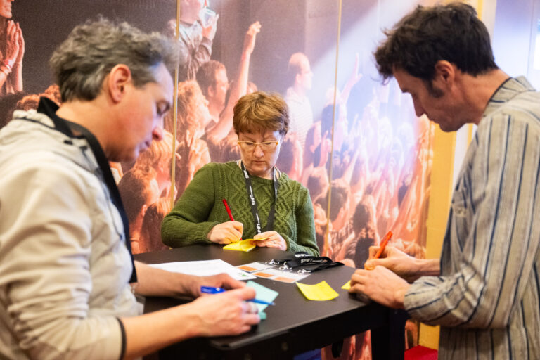 Drie personen staan aan een tafel en schrijven op post-its