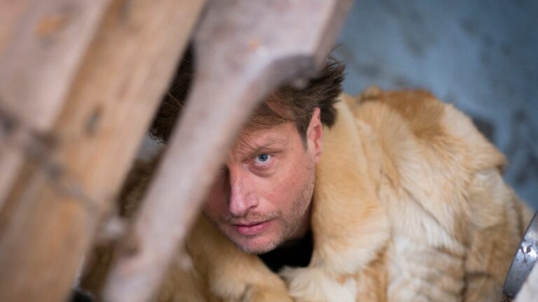 Man met bontjas aan kijkt naar boven door iets wat een groot gat in het plafond lijkt