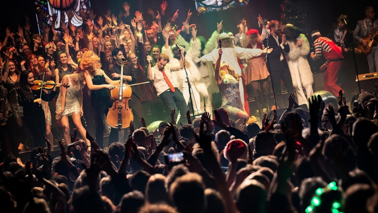Een bont gezelschap van muzikanten staat op het podium. onder hen zijn de zussen clean pete, die opgaan in de menigte van muzikanten. van achter zien wij het publiek helemaal los gaan