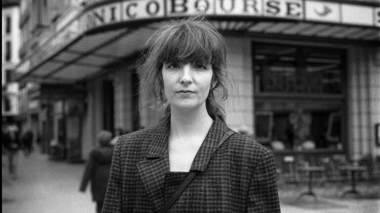 Zwart/wit foto jonge vrouw op straat met donker haar met pony en draagt een geruite blazer.