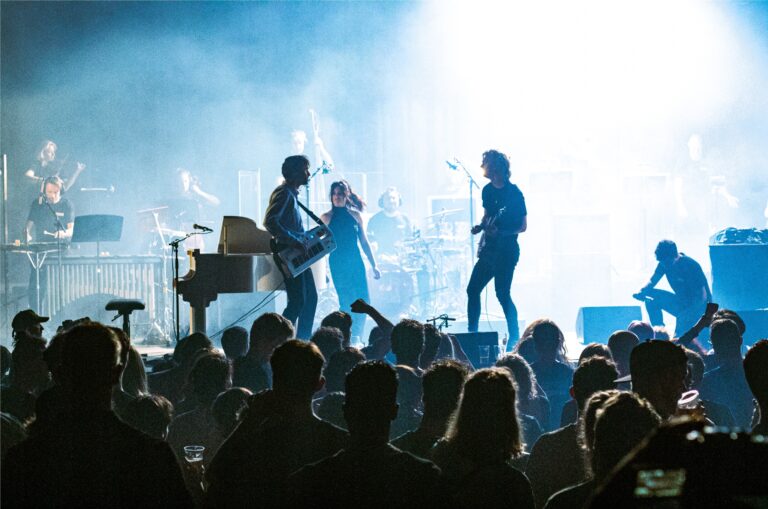 Live optreden van band Polyphonic op podium met blauwe en witte lichten.