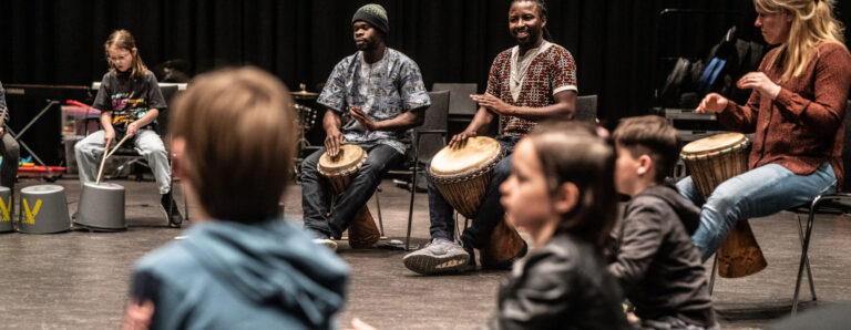 Een groep trommelaars maken muziek terwijl kinderen geanimeerd toekijken.