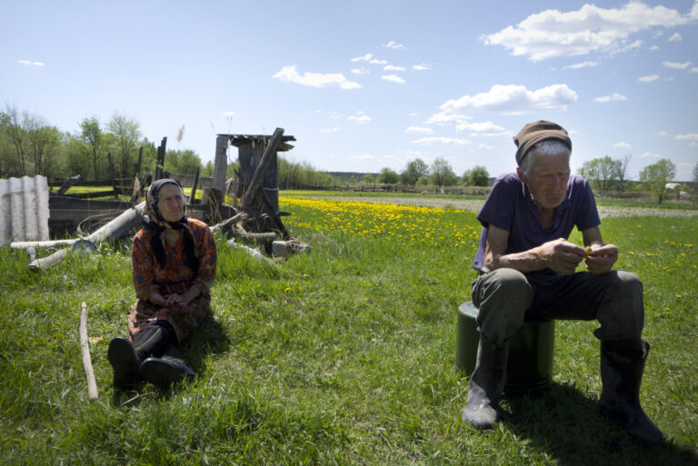 Oude man en vrouw zitten buiten in een graslandschaop