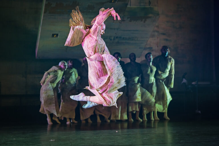 Danseres in losvallende roze jurk springt in de lucht met geheven voeten