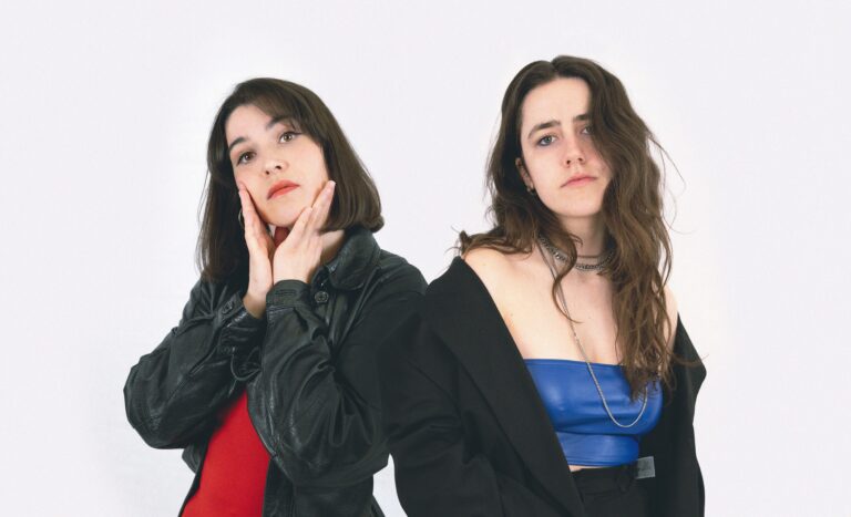 Twee jonge vrouwen donker haar staan vanaf heup op de foto in zwarte blouse en een rode en een blauwe top.