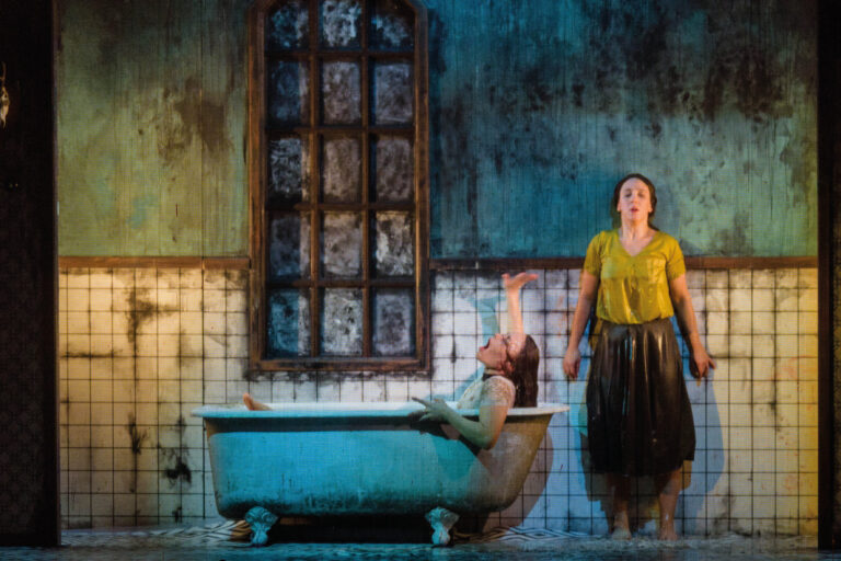 Vrouw in bad met hand om hoog en een vrouw tegen de verweerde muur