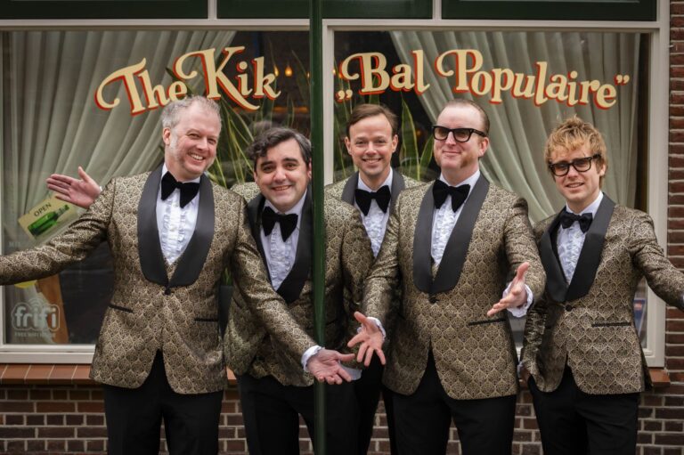 Vijf mannen 50-plus in pak met vlinderdas lachen met open armen.