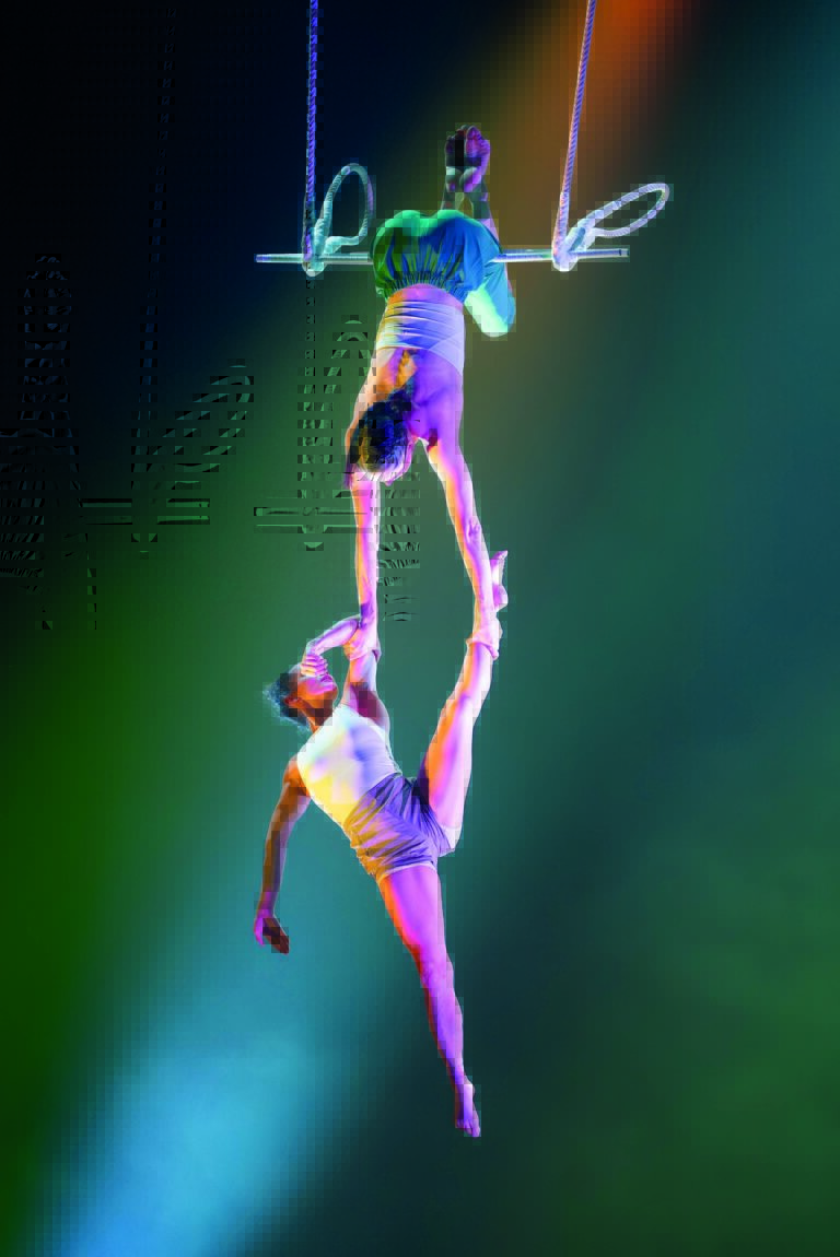 Een circusartiest hangt aan de trapeze en houdt een andere artiest vast