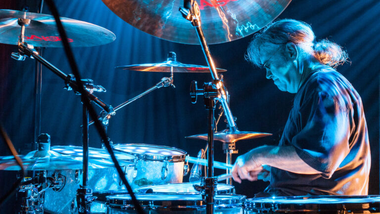 Ian Paice achter een drumstel vanuit zijperspectief met blauwe verlichting