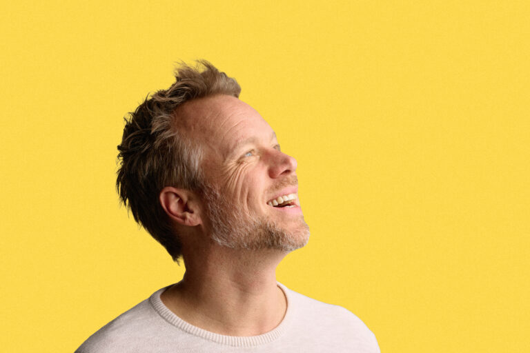 Man blond haar en baardje in wit shirt en gele achtergrond