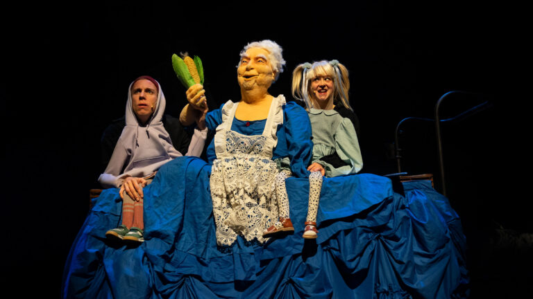 Drie vrouwen in historische kostuums staan op een theaterpodium.