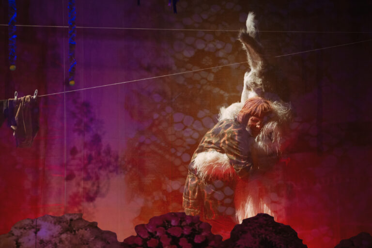 Twee personages, een in konijnenpak en een met roze pruik, knuffelen elkaar