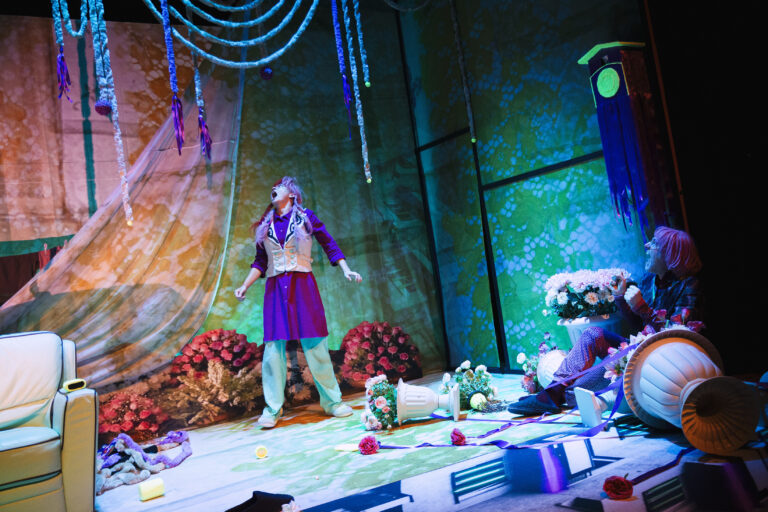 Meisje met roze pruik staat tussen een ravage op een podium