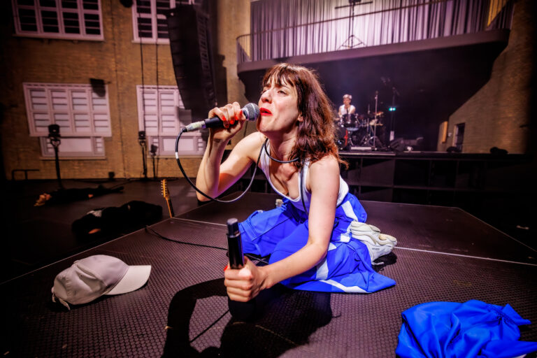 Zangeres in een blauwe jurk zingt in de microfoon op een podium.