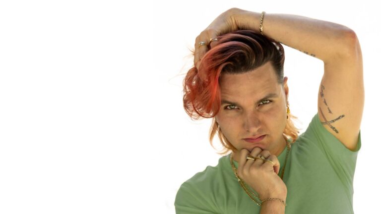 Man lang rood haar groen in T-shirt is geposeerd met hand op hoofd en hand op kin met witte achtergrond