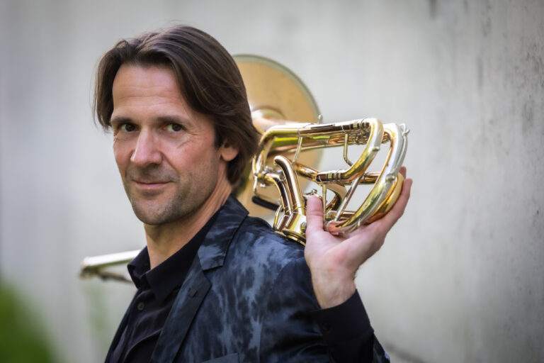 Brandt Attema met trombone in de nek, jasje aan, kijkt de camera in