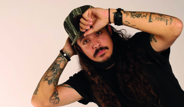 aaron boyd houdt zijn pet vast en heeft zwart t shirt aan, staat voor lichte achtergrond