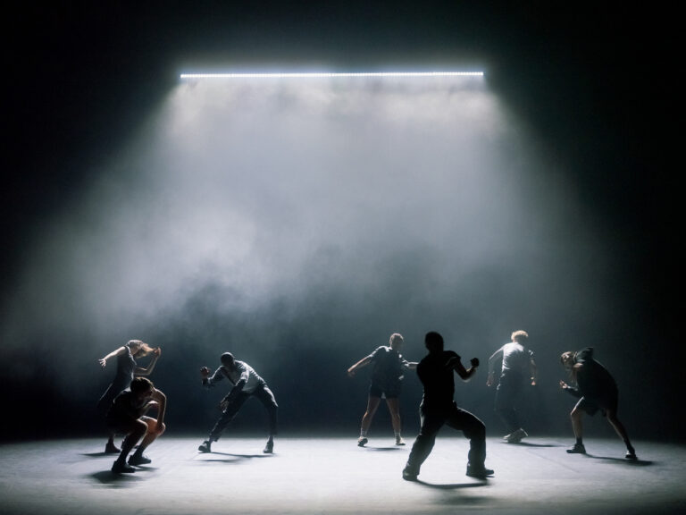 Dansers op donker podium met fel licht van boven
