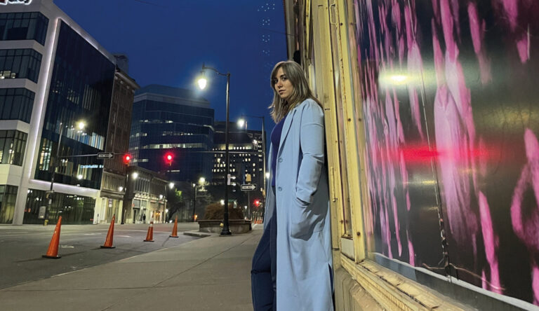 Actrice staat s'avonds onder een groot neon bord met daarop Alabama in een Amerikaanse straat