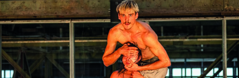 Danser zit op de schouders van een andere danser en knijpt haar gezicht samen