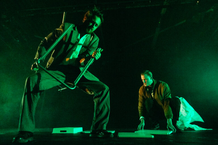 Twee muzikanten op een podium onder groen licht tijdens een live optreden.