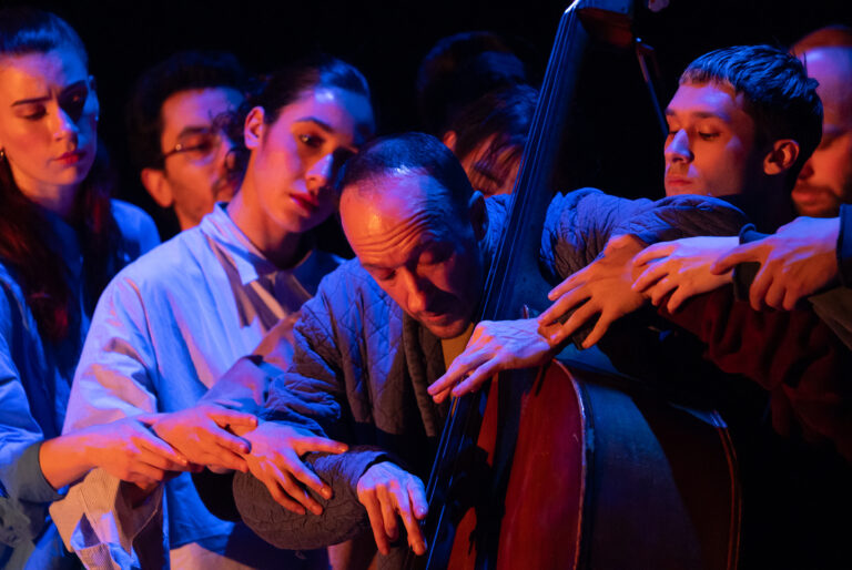Een groep muzikanten op een podium die een cello bespelen onder blauwe verlichting.