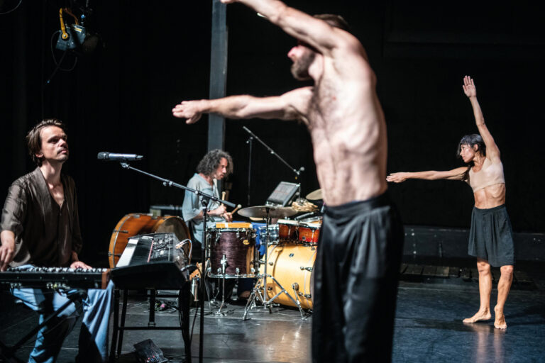 Dansers die met hun armen richting een aantal muzikanten wijzen