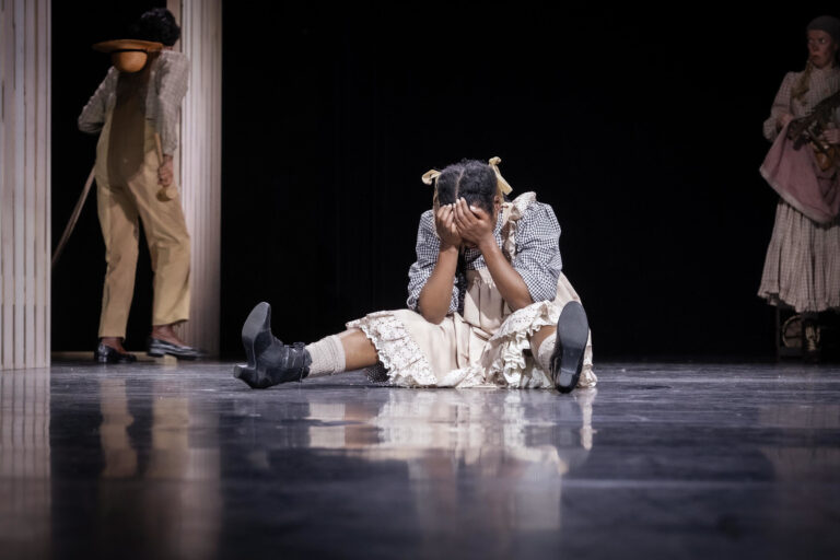 Meisje zit op de grond met haar benen gespreid en haar handen voor haar hoofd