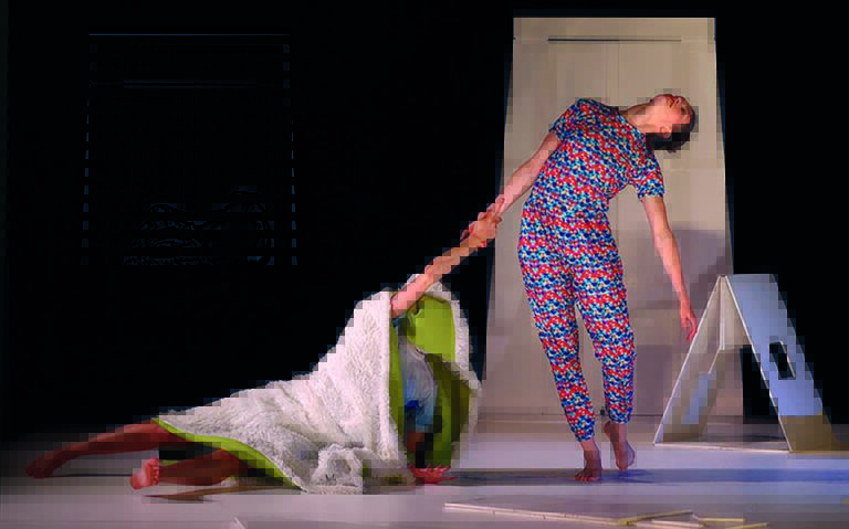 Danser in gekleurde kleding trekt aan groenedeken waar meisje in zeit