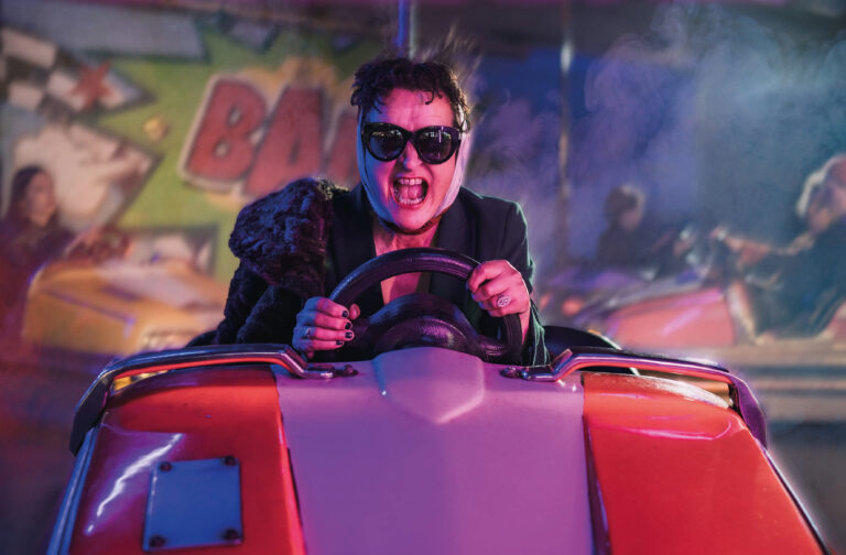 Man met zonnebril en doekje om hoofd zit achter het stuur in een botsauto