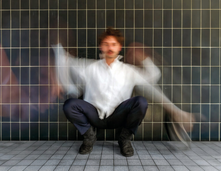 Donny Ronny zit gehurkt in een betegelde ruimte waarbij hij zijn armen zwaait.