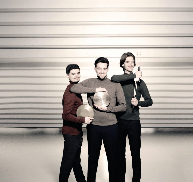 Drie mannen naast elkaar met instrumenten en horizontale strepen op de achtergrond