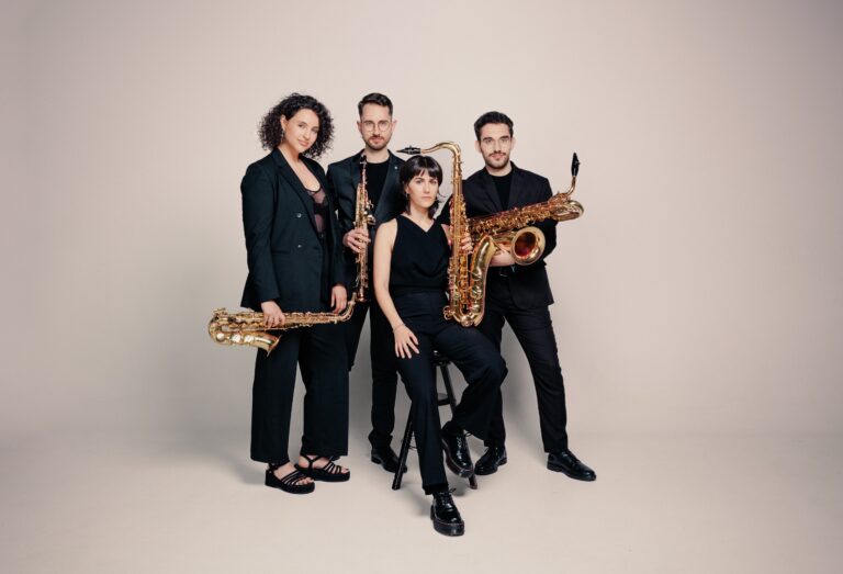 Twee mannen en Twee vrouwen die met hun muziekinstrumenten op de foto staan gekleed in zwart