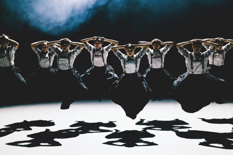 Dansers springend in de lucht met hun benen gebogen naar binnen, ze hebben allemaal zwart-witte volksoutfits aan