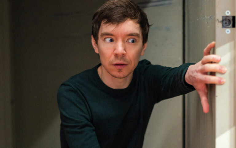 Fabian met een vervreemde blik met beide handen op een deur