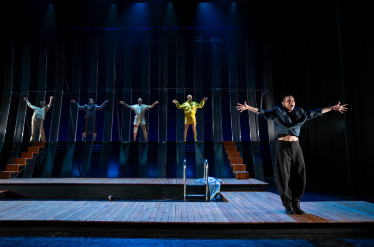 Vijf mensen op een podium, allemaal met de handen omhoog middenin een zang moment