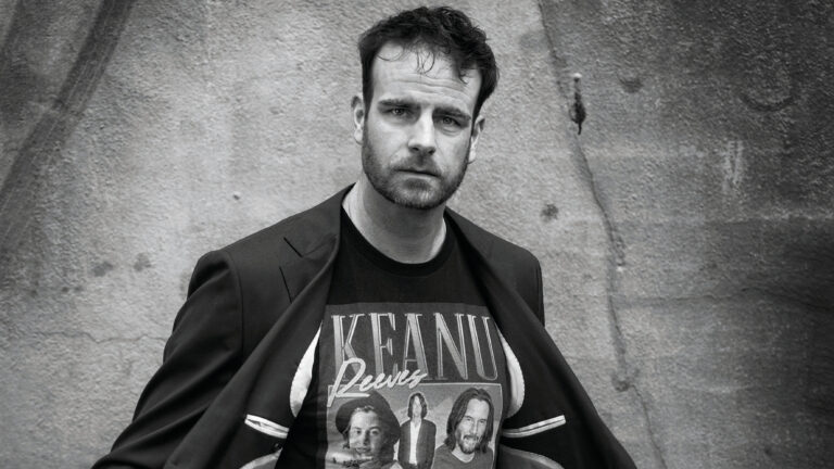 Henry in zwart/wit foto met zijn jasje open en een vintage Keanu Reeves t-shirt aan