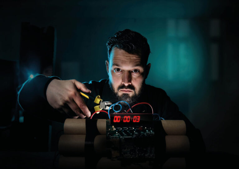 Jasper zit in het donker met een tang en staat op het punt een draadje bij een explosief door te knippen