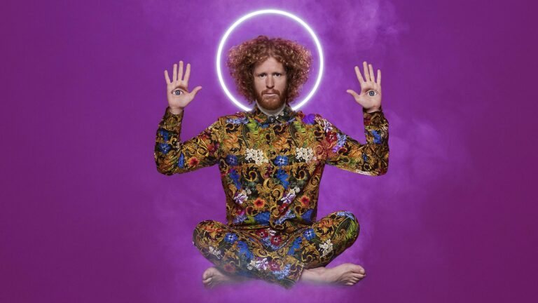 Een man in een kleurrijk, bloemig patroon zit in een meditatieve houding met een stralende halo achter zijn hoofd, op een paarse achtergrond.