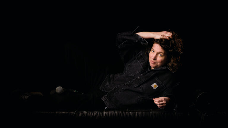 Kim ligt in donkere kleding op haar zij met een microfoon tussen haar benen